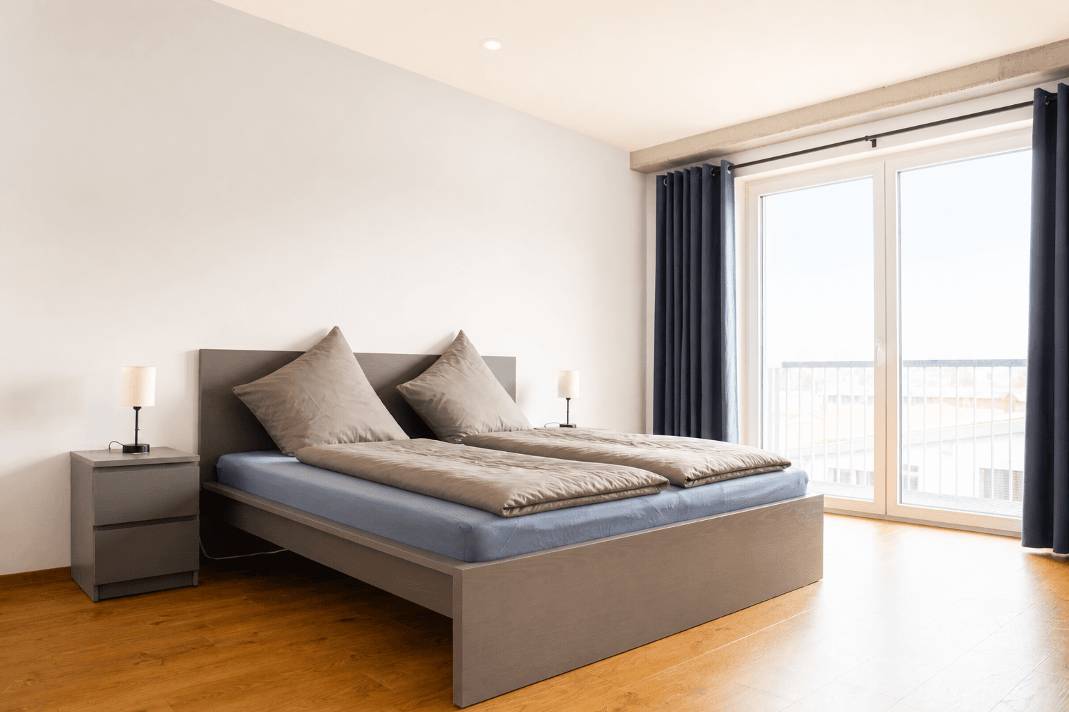 Schlafzimmer mit Doppelbett, anthrazit-blauen Verdunkelungsvorhängen und Balkontür