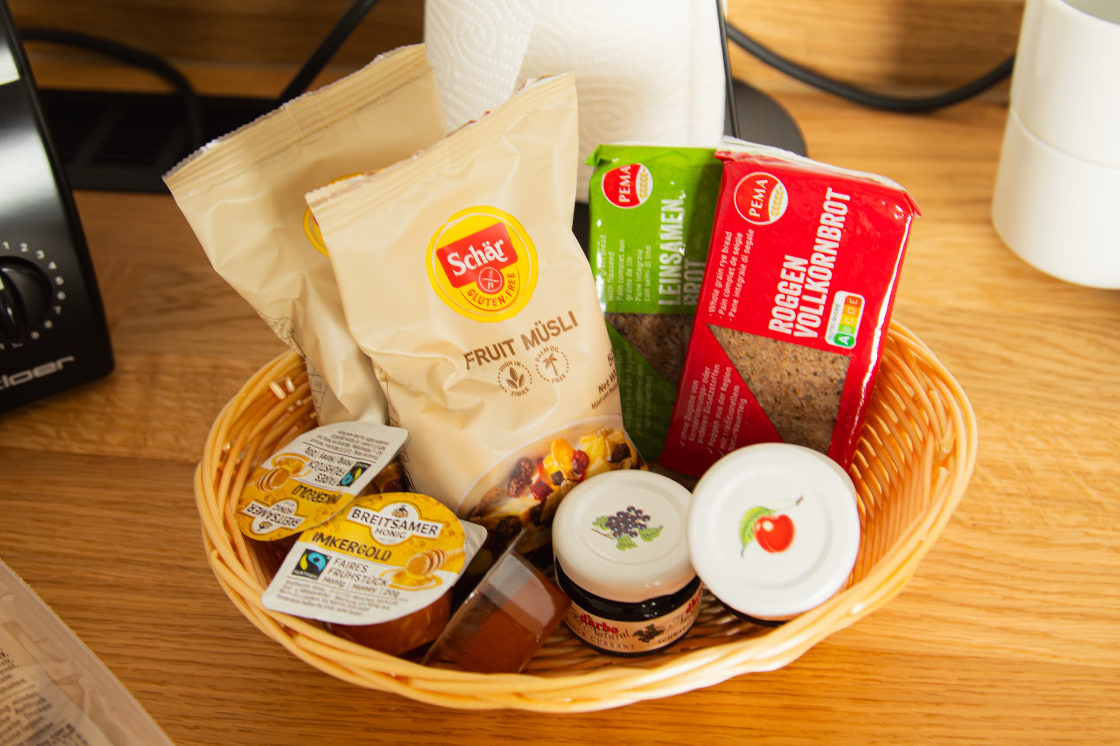 Korb mit Schär-Müsli, Roggenvollkornbrot, Honig und Marmeladen