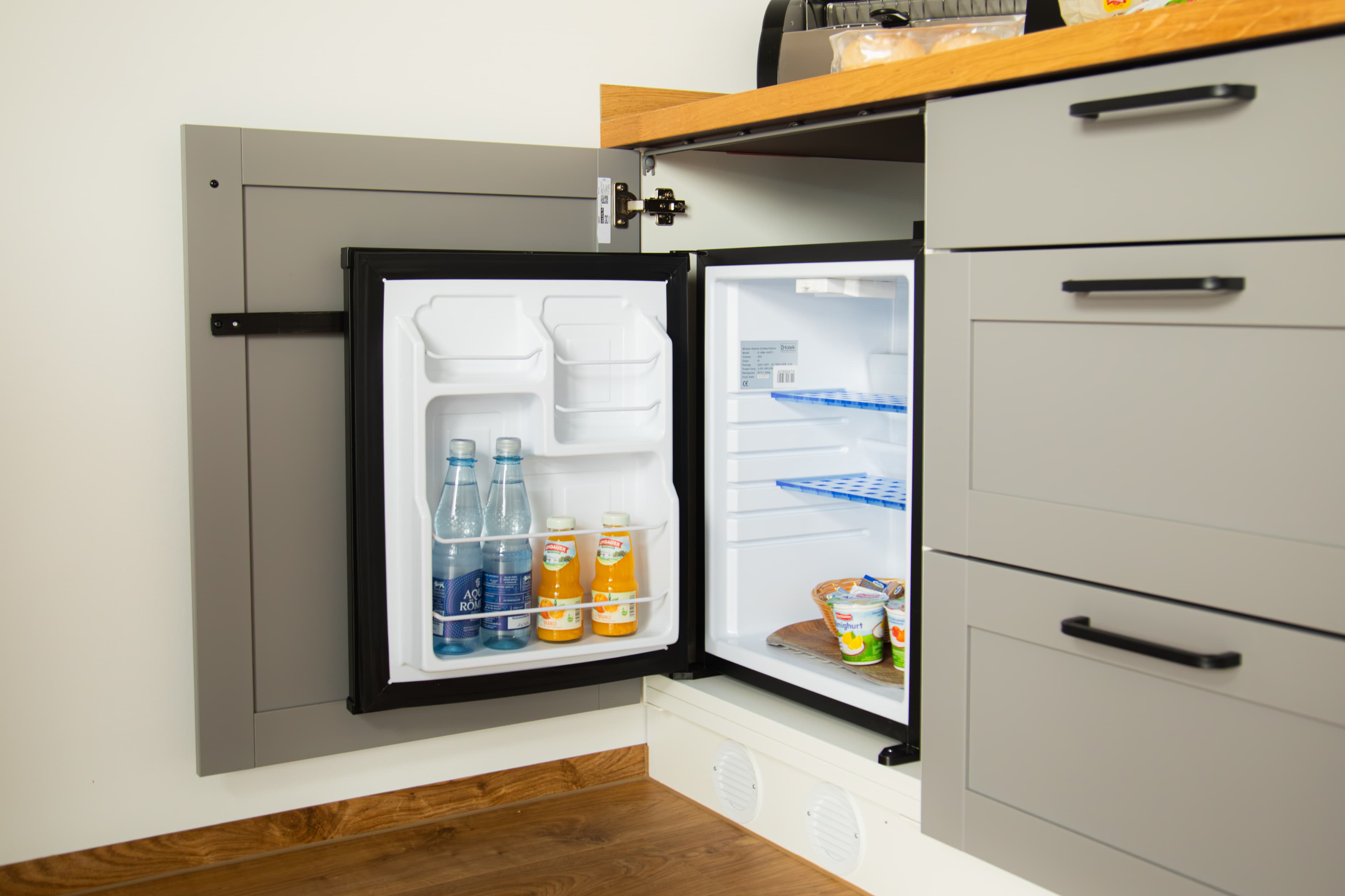Mini-Kühlschrank-Einbau in der Küchenzeile geöffnet mit Wasser und Saft