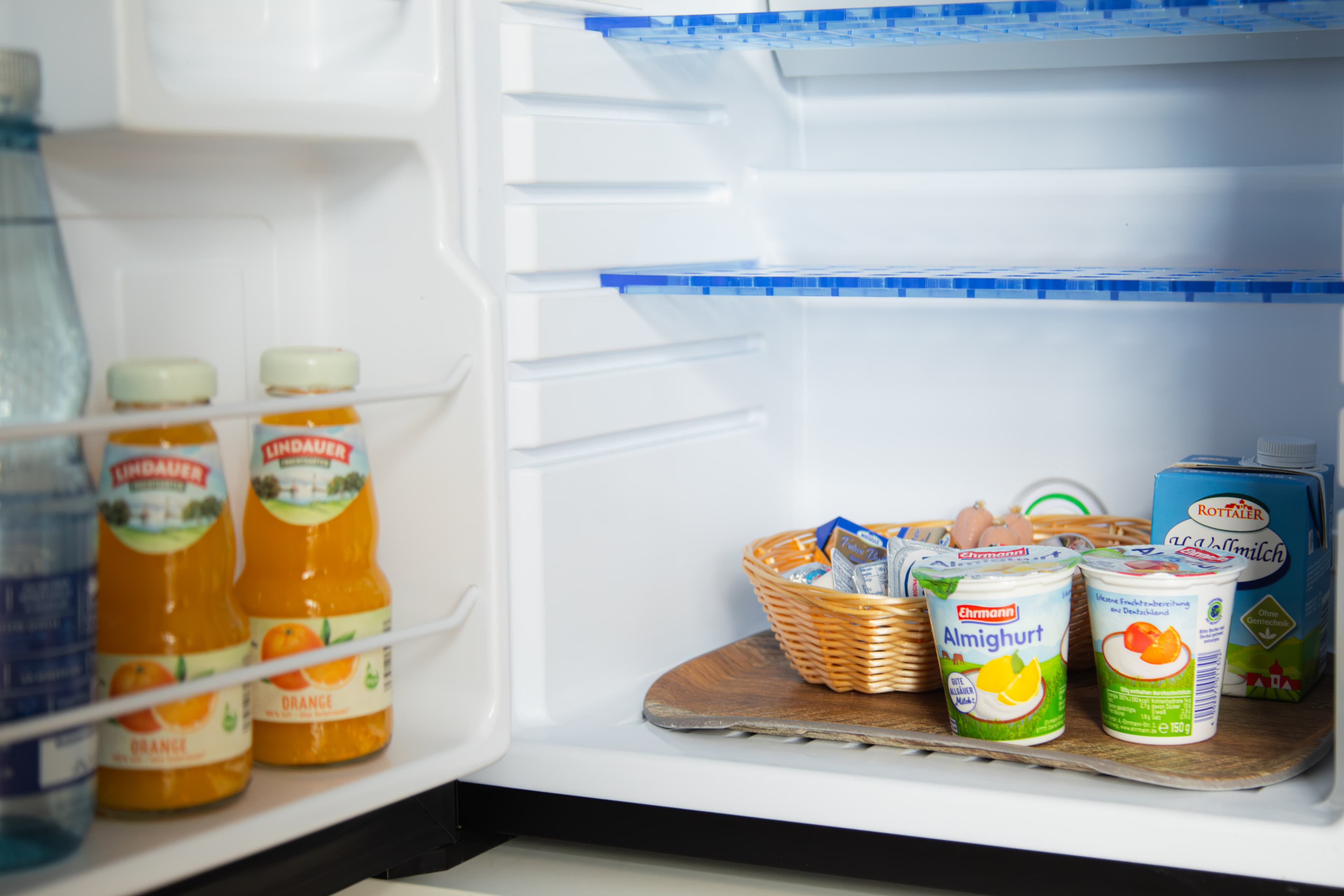 Geöffneter Kühlschrank mit Lindauer Orangensaft, Wasser, Aufschnitt-Korb und Milch